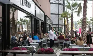 Gente disfrutando en los restaurantes de la torre outlet, rodeados de palmeras y flores.