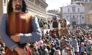 Gigantes y cabezudos desfilan entre una multitud en una plaza. Las figuras de cartón piedra, algunas con coronas, son el centro de atención.