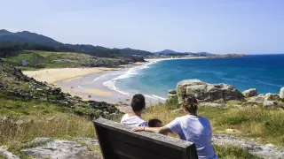 Familia contemplando la costa de las Rías Baixas que ver, con una playa dorada y el mar azul.