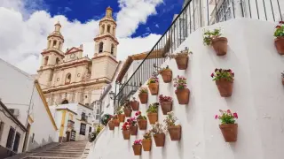 Un pueblo blanco andaluz con una iglesia imponente y macetas de flores adornando una pared. ¡Un lugar ideal que ver en Andalucía!