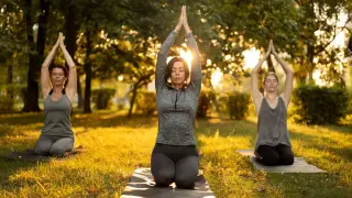 Tres mujeres meditan en un parque al atardecer, disfrutando de un retiro yoga Galicia.