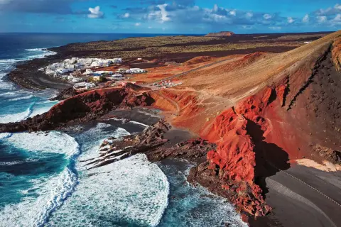 Vista aérea de El Golfo, Lanzarote. Un pueblo blanco junto a un cráter volcánico rojo y el mar azul. Imprescindible en tu lista de qué ver en Lanzarote.