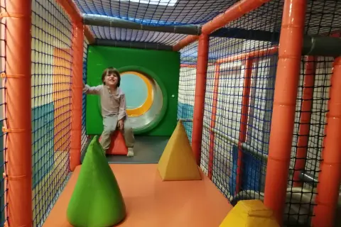 Niño sonriente en un divertido parque de bolas en Zaragoza, rodeado de redes y conos de colores.