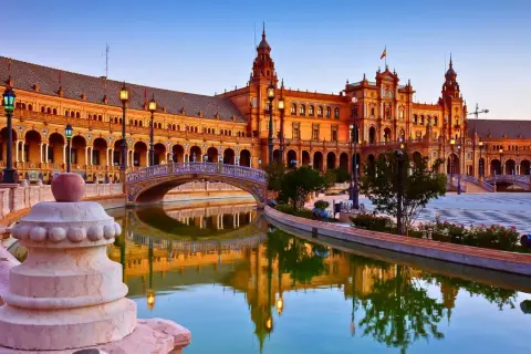 Plaza de España en Sevilla, una de las ciudades que ver en España. Reflejos dorados en el canal y un puente ornamentado.
