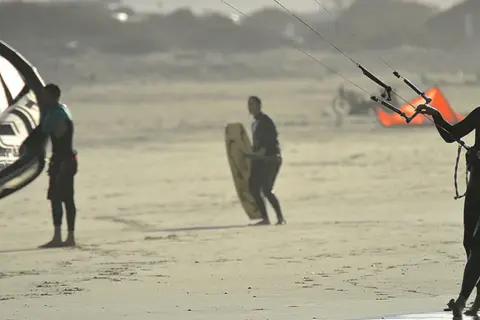 Hombres preparándose para el kitesurf en Lanzarote, con sus cometas y tablas listas para la acción en la playa.