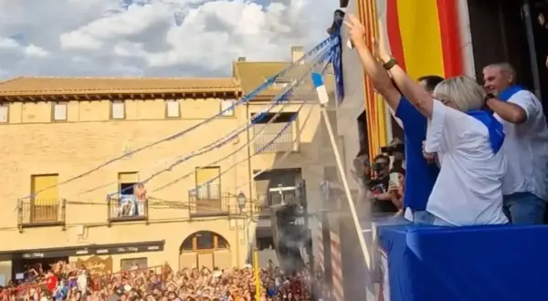 Gente celebra las fiestas de Utebo, ondeando banderas y lanzando confeti desde un balcón.