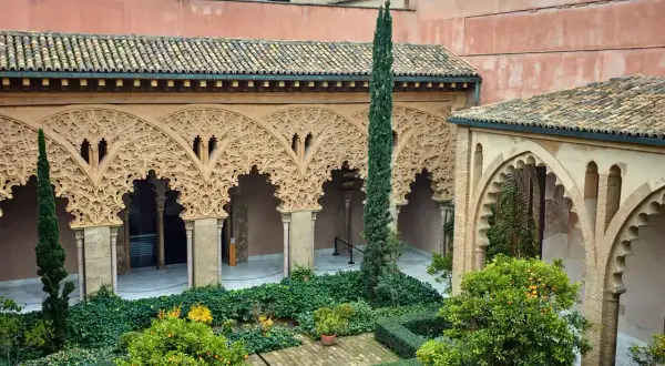 Patio de la casa de los Morlanes con arcos de yesería intrincada, vegetación exuberante y naranjos cargados de frutos.