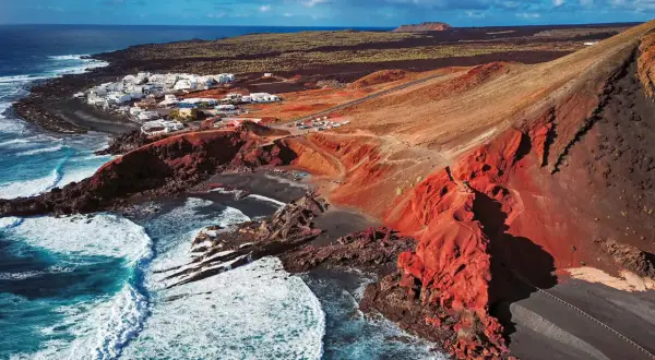 Vista aérea de El Golfo, Lanzarote. Un pueblo blanco junto a un cráter volcánico rojo y el mar azul. Imprescindible en tu lista de qué ver en Lanzarote.