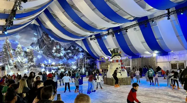Pista de hielo en Zaragoza, Plaza del Pilar, con un gran muñeco de nieve y gente patinando bajo un techo de telas azules y blancas.