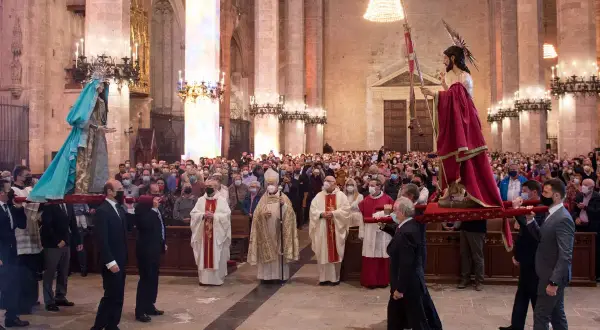 Procesión del Domingo de Resurrección en una catedral. Hombres portan imágenes religiosas mientras fieles observan.