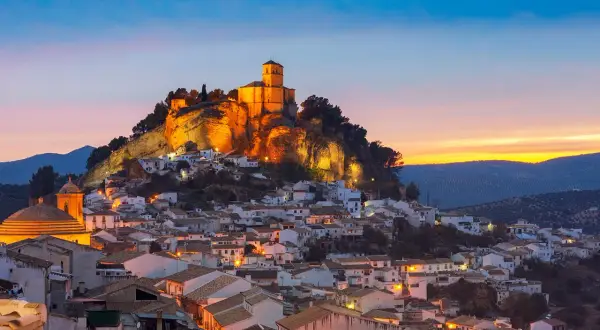 Pueblo blanco andaluz con castillo iluminado en la colina al atardecer. Un lugar encantador que ver cerca de Granada.