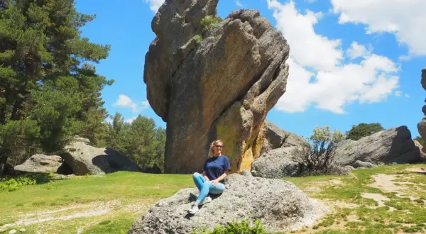 Mujer sentada en roca, con imponente formación rocosa detrás. Un paisaje natural que demuestra que merece la pena visitar Soria.