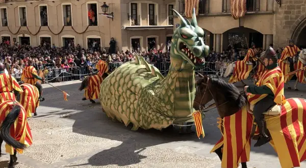 Un dragón gigante desfila en las fiestas de Alcañiz, acompañado por jinetes con trajes de rayas rojas y amarillas.
