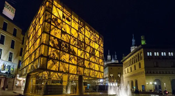 Edificio moderno y translúcido ilumina la noche junto a la fuente, cerca del museo del foro de Caesaraugusta.
