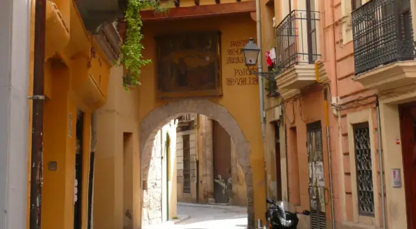 Calle estrecha con arco, fachadas amarillas y naranjas, un balcón y una moto. Descubre los **secret places Valencia**.