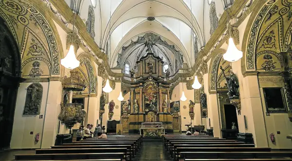 Interior de la iglesia de la Magdalena en Zaragoza, con bancos de madera, un retablo dorado y esculturas.
