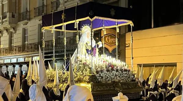 Procesión del Santo Entierro en Zaragoza. Figuras religiosas iluminadas por velas, rodeadas de nazarenos con túnicas y capirotes blancos.