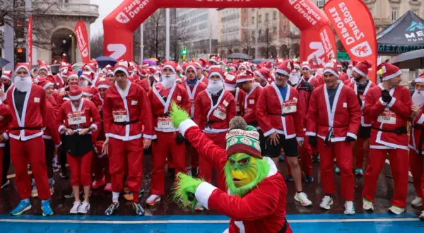 Multitud de personas disfrazadas de Papá Noel en Zaragoza, listas para una carrera. Un Grinch verde se une a la fiesta.