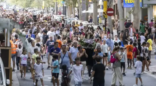 Multitud celebra las fiestas del barrio Las Fuentes en Zaragoza. Una procesión avanza por la calle con gente de todas las edades.