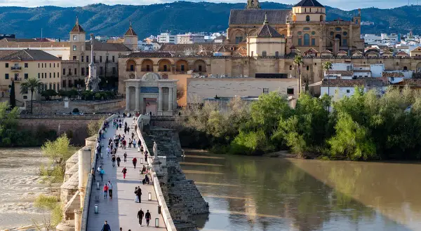 El Puente Romano de Córdoba, con la Mezquita-Catedral al fondo, es lo mejor de Córdoba. Gente pasea por el puente sobre el río Guadalquivir.