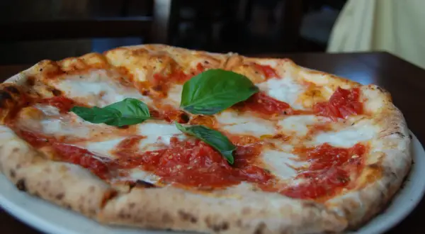Pizza margarita recién horneada, con tomate y mozzarella fundida, decorada con hojas de albahaca fresca. ¡Una delicia que te hará buscar las mejores pizzerías Zaragoza!