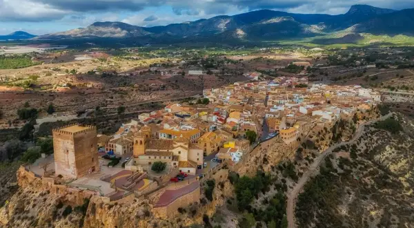 Pueblo blanco en un acantilado con castillo, ideal para saber qué ver en Murcia y alrededores. Paisaje montañoso al fondo.