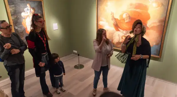 Un grupo de personas, incluyendo una niña, disfruta de una visita guiada en el **Día de los Museos Zaragoza**, admirando obras de arte.
