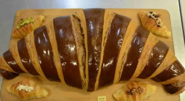 Un croissant gigante con glaseado de chocolate y pequeños croissants decorados, perfectos para un desayuno en Zaragoza.