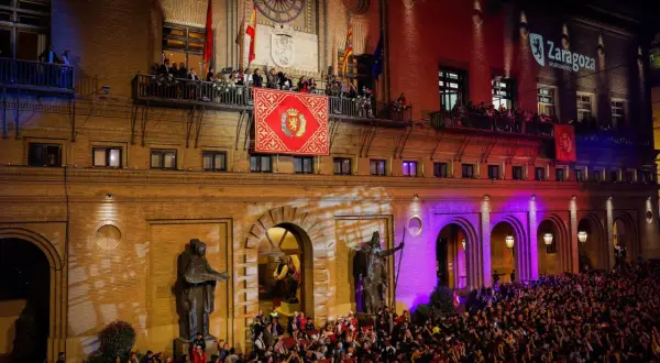 Multitud celebra el pregon de pilares en Zaragoza. Gente en balcones y plaza, luces y banderas.