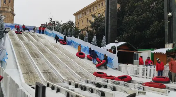 Diversión en los trineos de la Plaza del Pilar. Niños y adultos disfrutan de un tobogán nevado, con la Basílica de Nuestra Señora del Pilar de fondo.