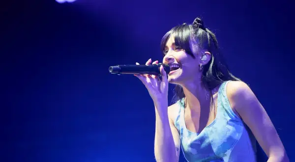 Aitana Zaragoza canta con pasión en un concierto, iluminada por luces azules.
