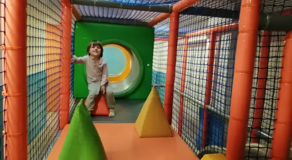 Niño sonriente en un divertido parque de bolas en Zaragoza, rodeado de redes y conos de colores.