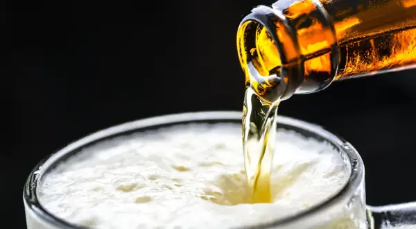 Cerveza dorada cayendo de una botella a un vaso espumoso. ¡Una birra Zaragoza perfecta para refrescarse!