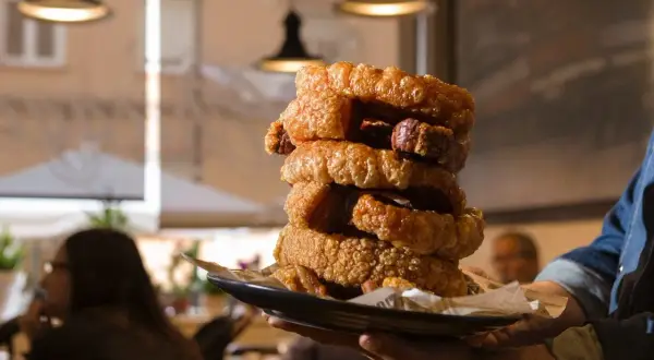 Torre de torrezno crujiente, ¡el mejor torrezno de Zaragoza! Servido en plato negro, listo para disfrutar.
