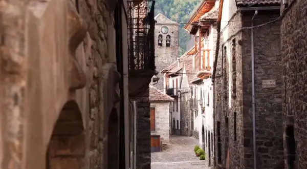 Calle empedrada en un pueblo de Aragón, con casas de piedra y un campanario al fondo.