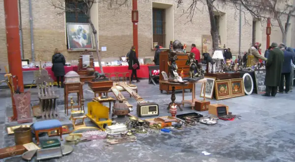 Mercadillo en la plaza San Bruno con antigüedades, muebles y objetos decorativos expuestos en el suelo y mesas.