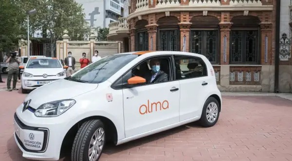 Un hombre con mascarilla conduce un coche blanco de carsharing en Zaragoza.