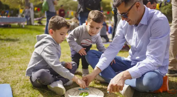 Un padre y sus hijos disfrutan de un juego en el césped, creando un momento familiar entre las tribus del parque Zaragoza.