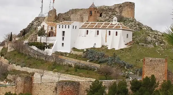 Iglesia Nuestra Señora de Gracia, un edificio blanco con tejado a dos aguas, se alza en una colina rocosa junto a ruinas de un castillo.