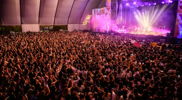 Multitud vibrante en concierto, con luces de escenario y carteles. Se aprecia la **autorización menores espacio Zity** en un cartel.