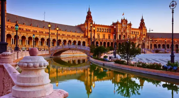 Plaza de España en Sevilla, una de las ciudades que ver en España. Reflejos dorados en el canal y un puente ornamentado.