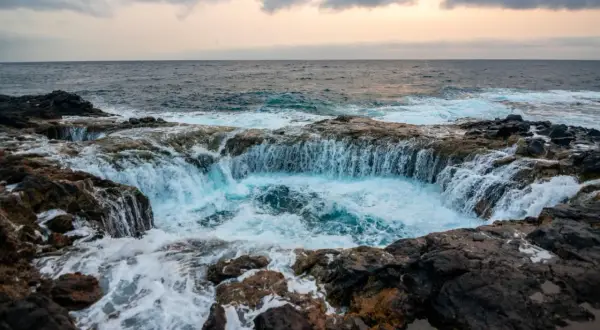 El mar choca contra las rocas volcánicas, creando una cascada de agua azul en un agujero natural. Un lugar impresionante que ver en Gran Canaria.