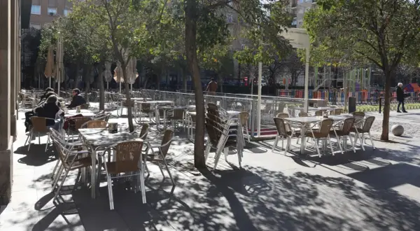Mesas y sillas vacías en la terraza de bares de la plaza San Francisco, bajo la sombra de los árboles.