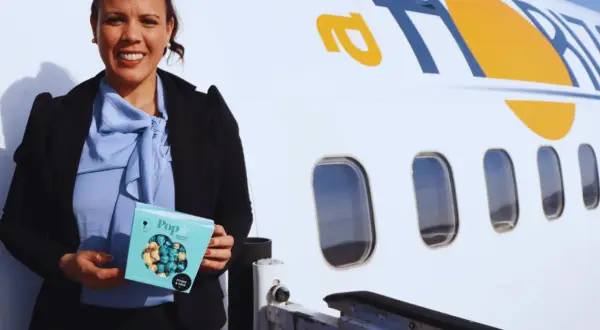 Mujer sonriente con caja de palomitas junto a un avión con el logo "air horizont".