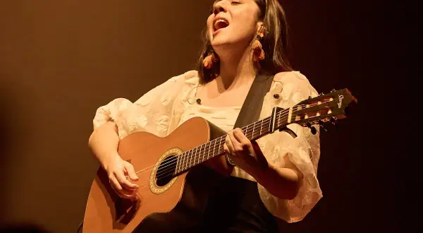 Valeria Castro Zaragoza canta con pasión, guitarra en mano, bajo una luz cálida.