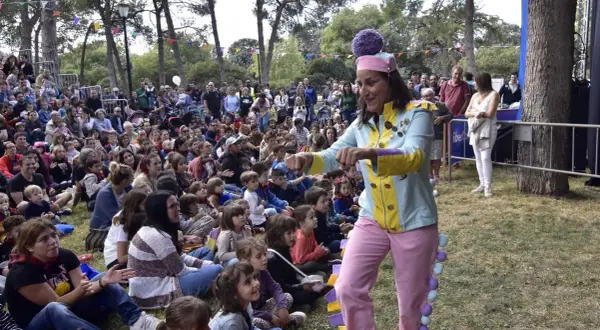 Actriz con traje colorido anima a niños en un espectáculo de marionetas en el parque.