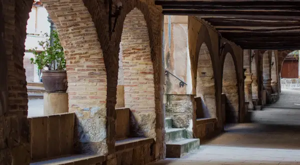 Pasaje abovedado de piedra y ladrillo con arcos, bancos de piedra y una planta en maceta. Un lugar con encanto para pasear y descubrir la fresneda que ver.
