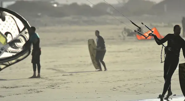 Hombres preparándose para el kitesurf en Lanzarote, con sus cometas y tablas listas para la acción en la playa.