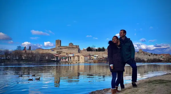 Pareja disfruta de la vista del río Duero y la ciudad de Zamora, un lugar que merece la pena visitar. Patos nadan en el agua azul.