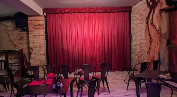 El escenario de el.sotano magico, con cortinas rojas y sillas metálicas, listo para un espectáculo.